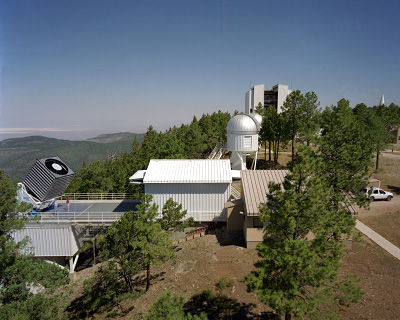 Apache Point Observatory: Apache Point Observatory in the Sacramento Mountains of New Mexico. The Sloan Digital Sky Survey's 2.5-meter telescope is on the left. White Sands National Monument is visible in the distance, above the telescope. The monitor telescope, used for calibrations, is inside the small dome to the right of center. Optical fibers for spectroscopy are pre-positioned each day in the building on the right (behind the trees). The building in the center rolls on rails to cover the 2.5-meter telescope when it is not in use.