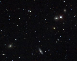 SDSS First Light: A small section of the first-light image obtained by the Sloan Digital Sky Survey on the night of May 27-28, 1998. The overall image is over 5,000 times larger than this small piece of the constellation Serpens. The photo was assembled from digital scans taken through separate filters. (The individual colors provide valuable information for identifying the objects.) It also shows stars in our own Galaxy (the brighter ones are recognizable by the cross pattern), a half-dozen distant galaxies near enough to show morphological features like disks and rings, and many fainter and farther galaxies, distinguished from stars by their slightly fuzzy appearance.