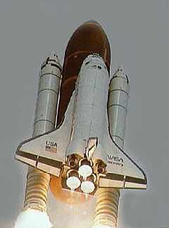 Launch of Space Shuttle for the Deployment of the NASA/ESA Hubble Space Telescope: With the Hubble Space Telescope on board, Discovery begins its roll maneuver after liftoff from Kennedy Space Center on April 24, 1990. This low-angle view of the launch shows the shuttle atop the external tank, flanked by two solid rocket boosters, as it rises into the sky.