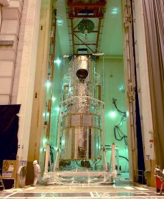 Image Title: Hubble is lifted into the upright position in Lockheed Martin's acoustic vibration chamber in preparation for its 1990 launch aboard the space shuttle Discovery. The telescope was designed and built in the 1970s and 1980s, but its launch was delayed by the space shuttle Challenger disaster in 1986. A close look at this image reveals a portion of the 225 feet (68.6 m) of handrails installed around the outside for astronauts to grip during repair mission spacewalks.