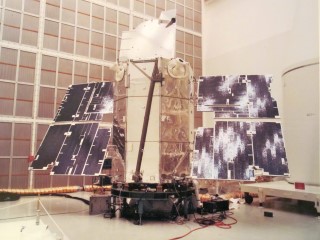 The First Successful Oribiting Astronomical Observatory: OAO-2 operated from 1968 to 1972 and obtained low-resolution UV spectra and broad-band photometric observations of many classes of astronomical objects.  The 2012 kg satellite is shown here in a clean room at the Goddard Space Flight Center. The panels on the two sides of the main body of the satellite are the solar panels that power the system. The telescopes are mounted inside the cylindrical structure. For scale, compare the size of the observatory to the persons in clean suits in the lower right of the image.